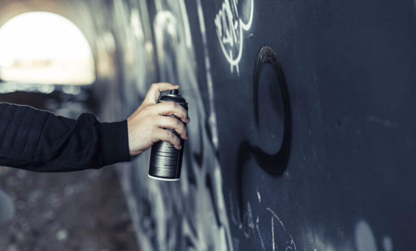 Una persona haciendo un graffiti negro en una pared oscura.